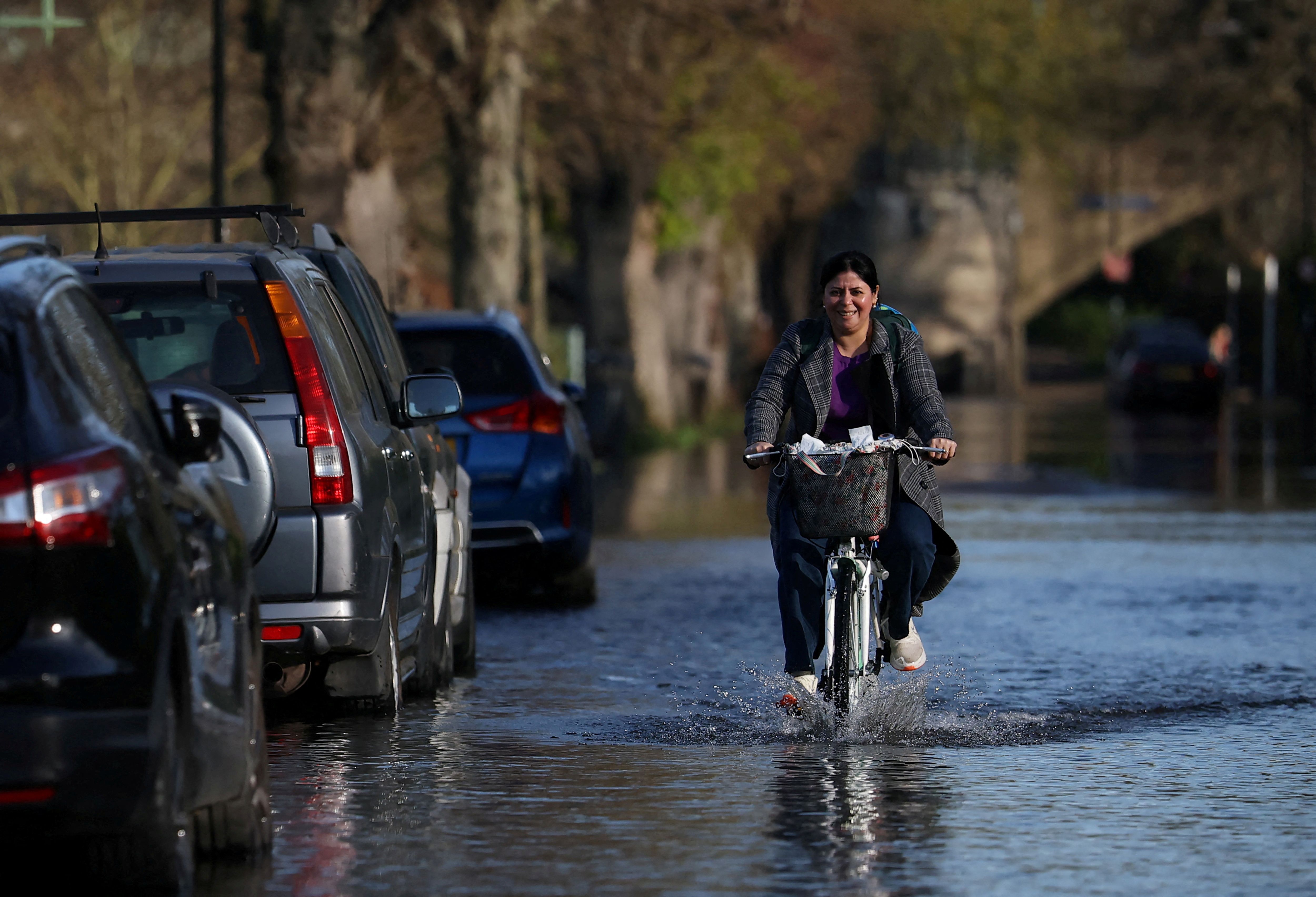 A person cycles along a flooded road after the overtopping of the River Thames.