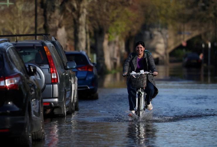 A person cycles along a flooded road after the overtopping of the River Thames.
