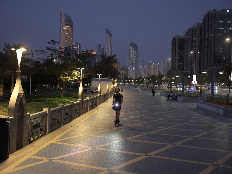 A person rides a scooter with the skyline visible in the background, in Abu Dhabi, United Arab Emirates.