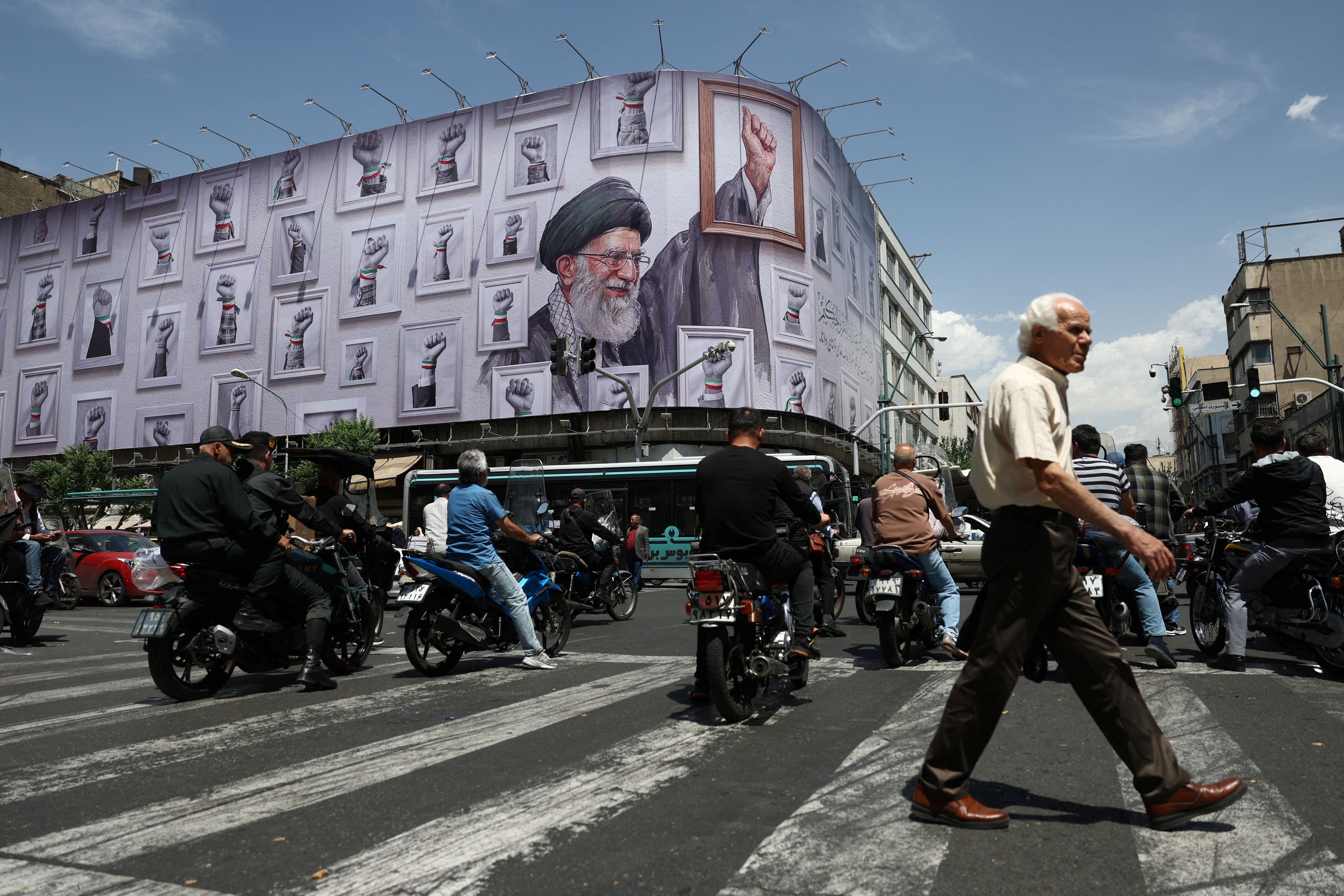 Varias personas circulan en motocicleta cerca de una valla publicitaria en Teherán que muestra una imagen del difunto Líder Supremo de Irán, el ayatolá Ali Khamenei.