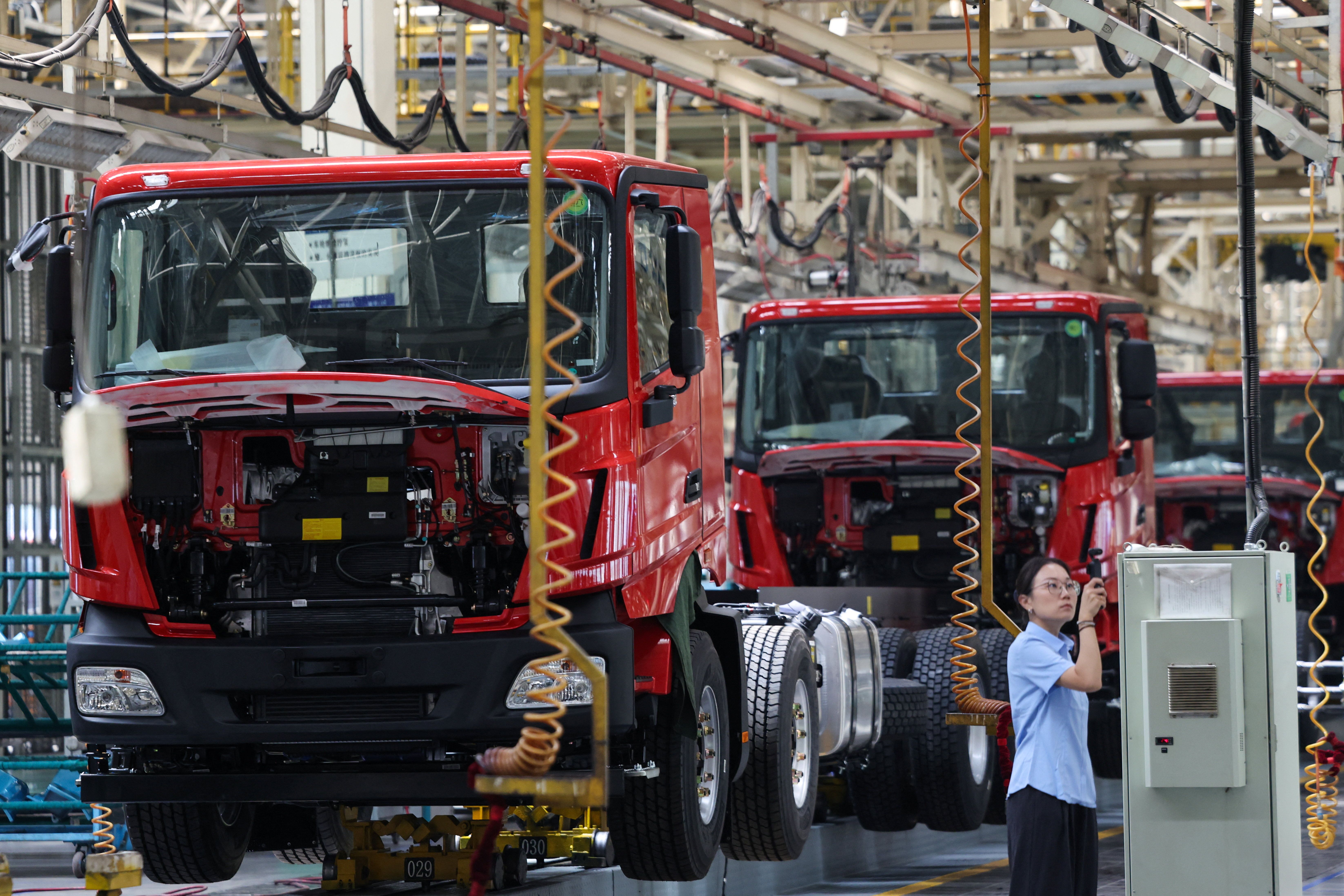 A woman films next to a truck assembly line at Beiben Trucks Group factory during an organised media tour, in Baotou.