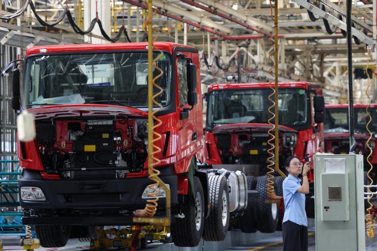 A woman films next to a truck assembly line at Beiben Trucks Group factory during an organised media tour, in Baotou.