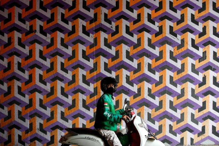 A man wears a mask, astride a motorbike.