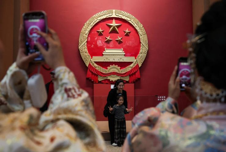Women take photos of China’s national emblem