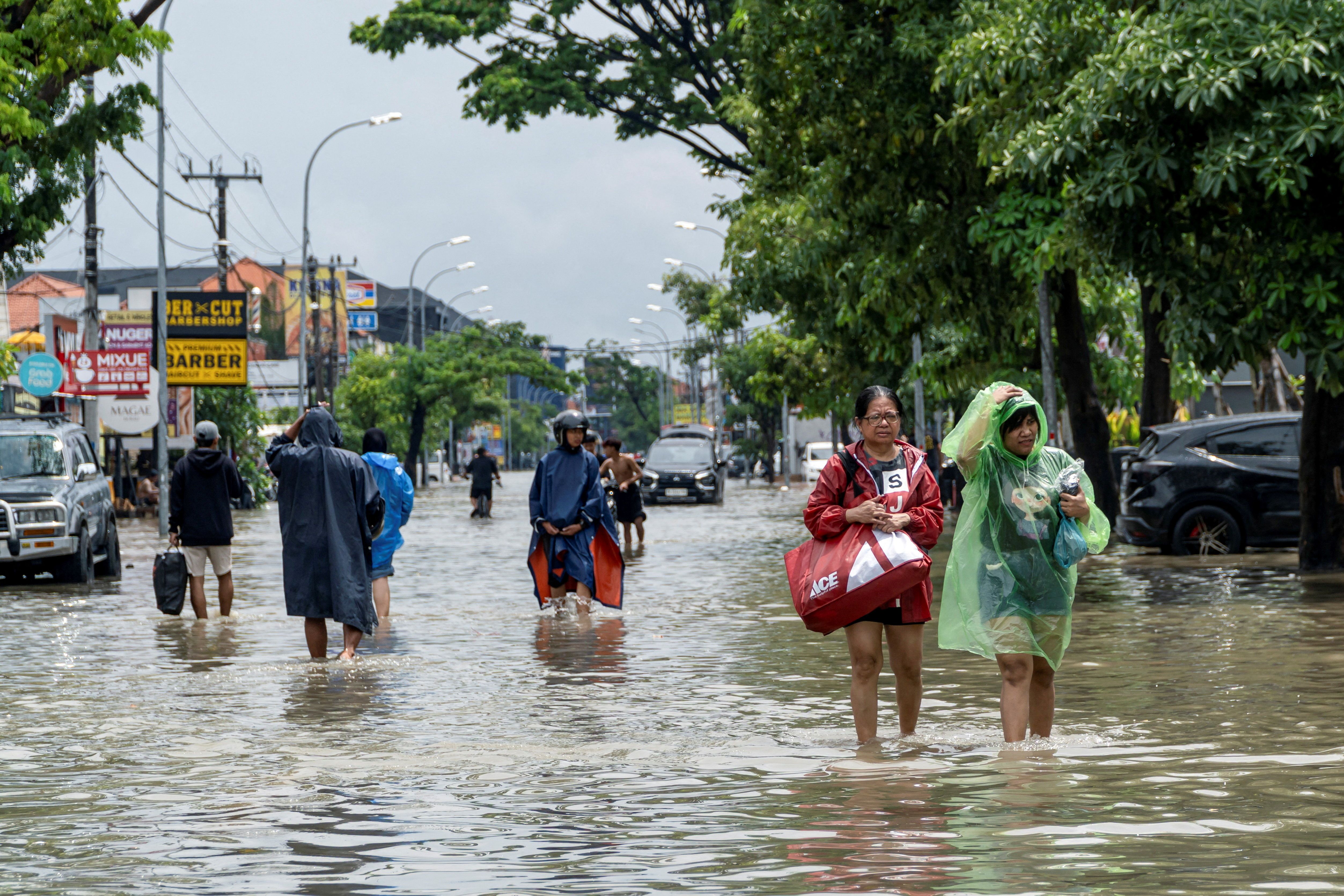 People carrying their belongings wade through a flooded street in Bali.