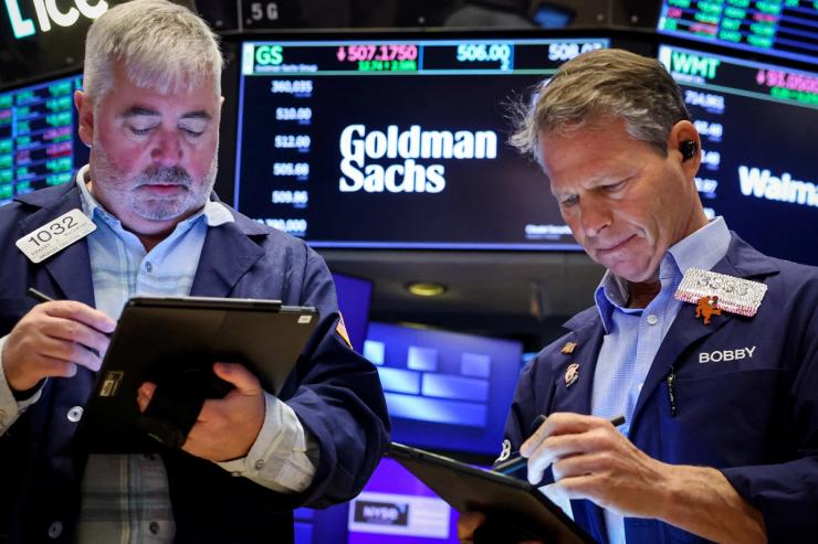 Traders work on the floor, as a screen displays The Goldman Sachs logo and trading information.