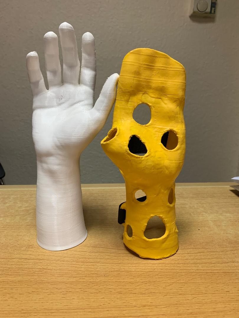 A white model of a hand sits upright next to a yellow glove-like rubber cast.