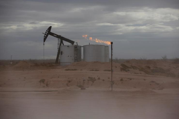 Dust blows around a crude oil pump jack and flare burning excess gas at a drill pad.
