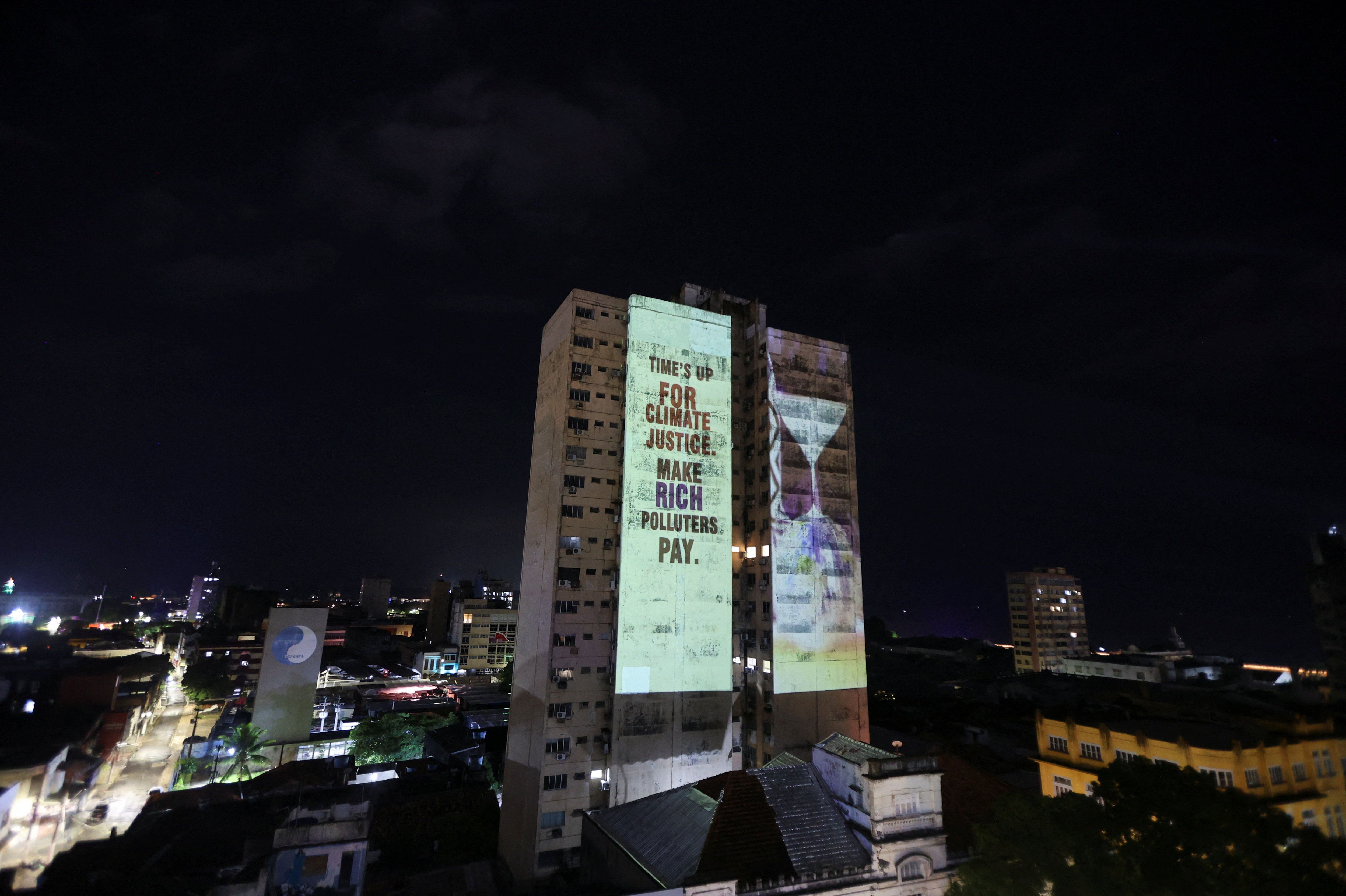 A message is projected on a building during a demonstration by OXFAM at COP30.