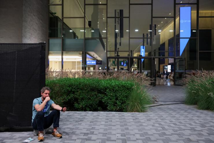A journalist uses his phone as he sits outside the media center, while draft of COP28 deal is negotiated, during the United Nations Climate Change Conference (COP28).
