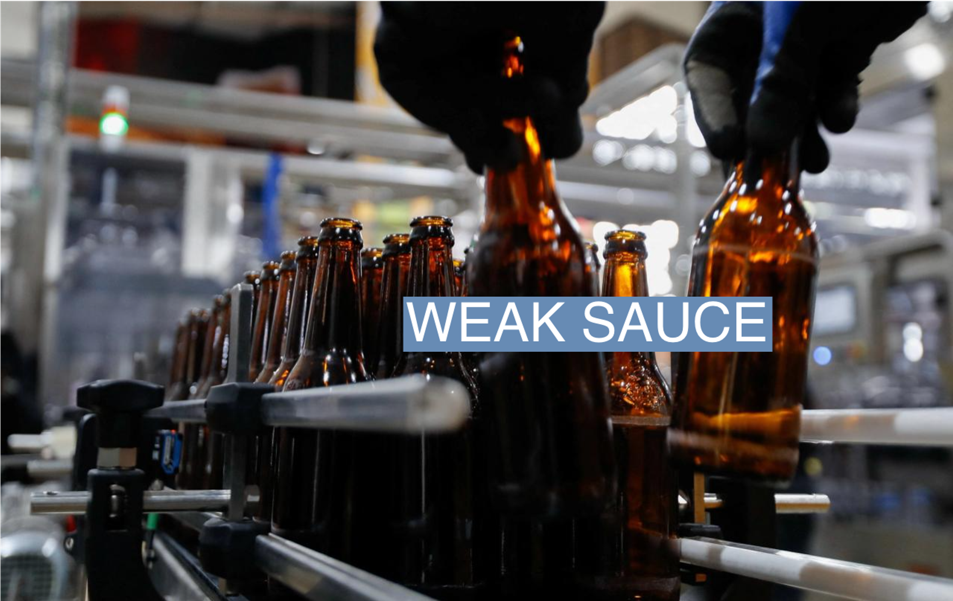 An employee arranges beer bottles on a conveyor belt along a brewery production line.