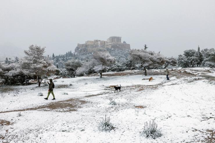 People and their dogs make their way on Pnyka hill, as the Parthenon temple is seen in the background, during snowfall in Athens, Greece, February 6, 2023.