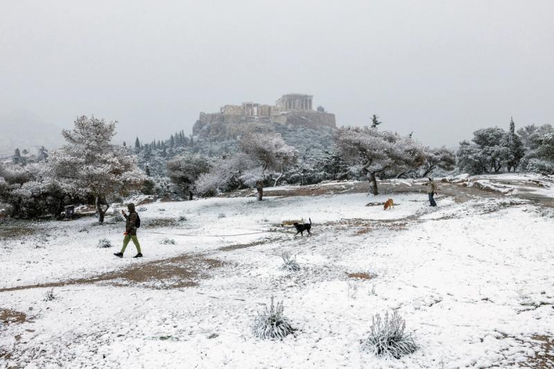 People and their dogs make their way on Pnyka hill, as the Parthenon temple is seen in the background, during snowfall in Athens, Greece, February 6, 2023.