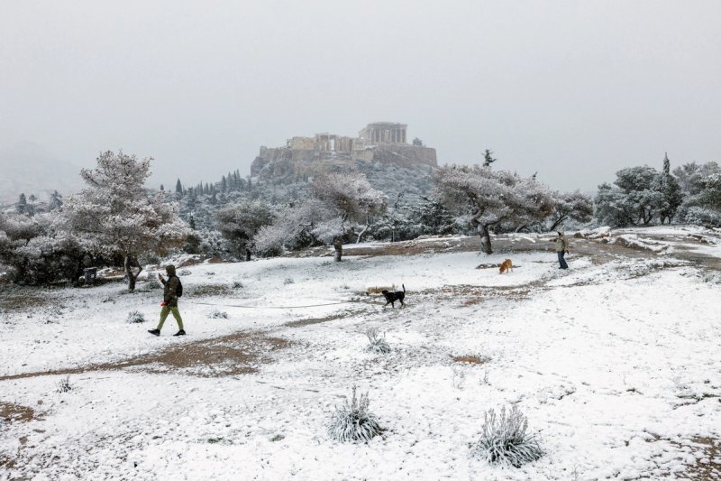 People and their dogs make their way on Pnyka hill, as the Parthenon temple is seen in the background, during snowfall in Athens, Greece, February 6, 2023. 