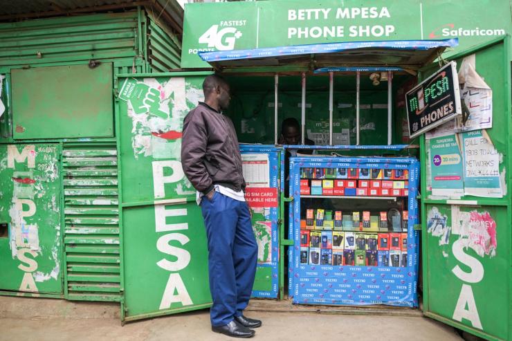 A customer outside a kiosk next to a sign advertising M-Pesa, Safaricom’s mobile money service, in Nairobi.