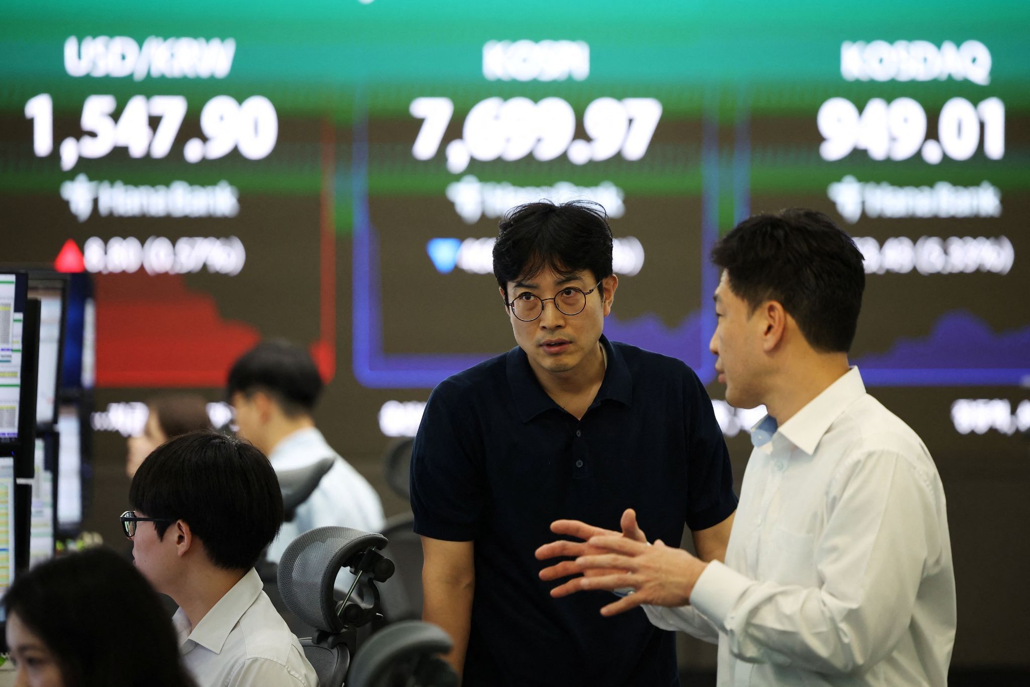 Currency dealers talk in front of an electronic board displaying the exchange rate between the U.S. dollar and South Korean won. 