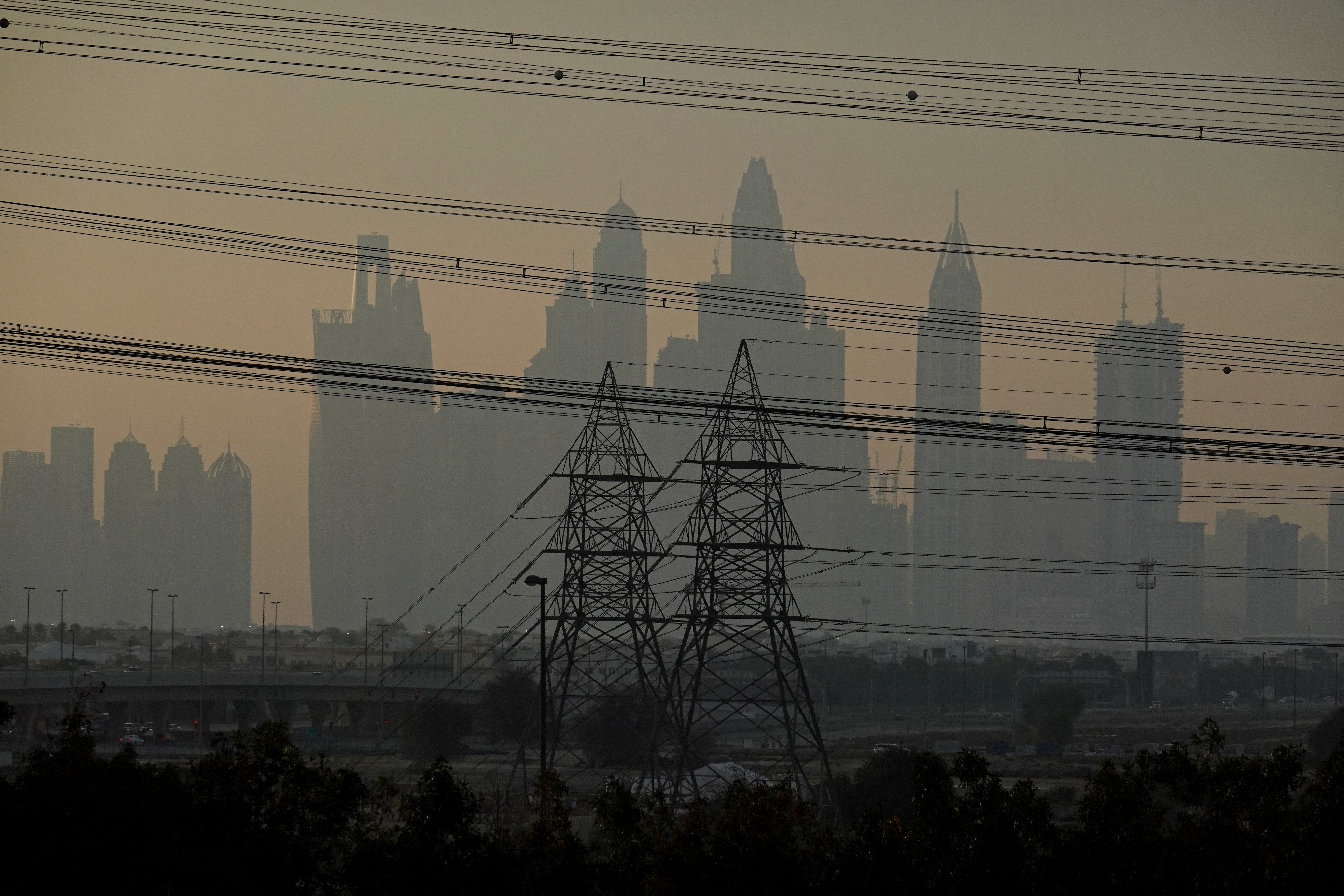 Power towers and cables with the Dubai skyline in the background.