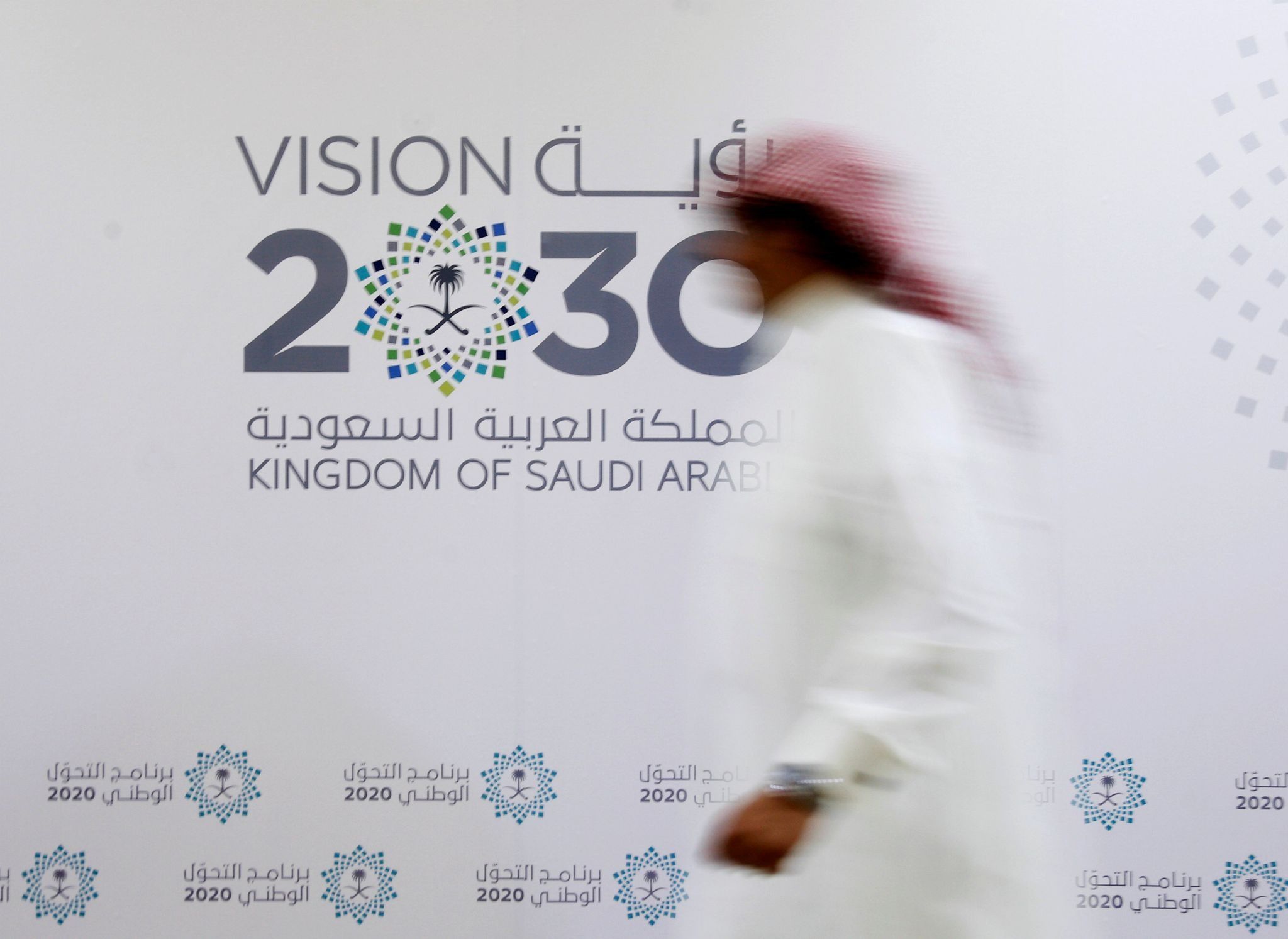 A Saudi man walks past the logo of Vision 2030 after a news conference in Jeddah.