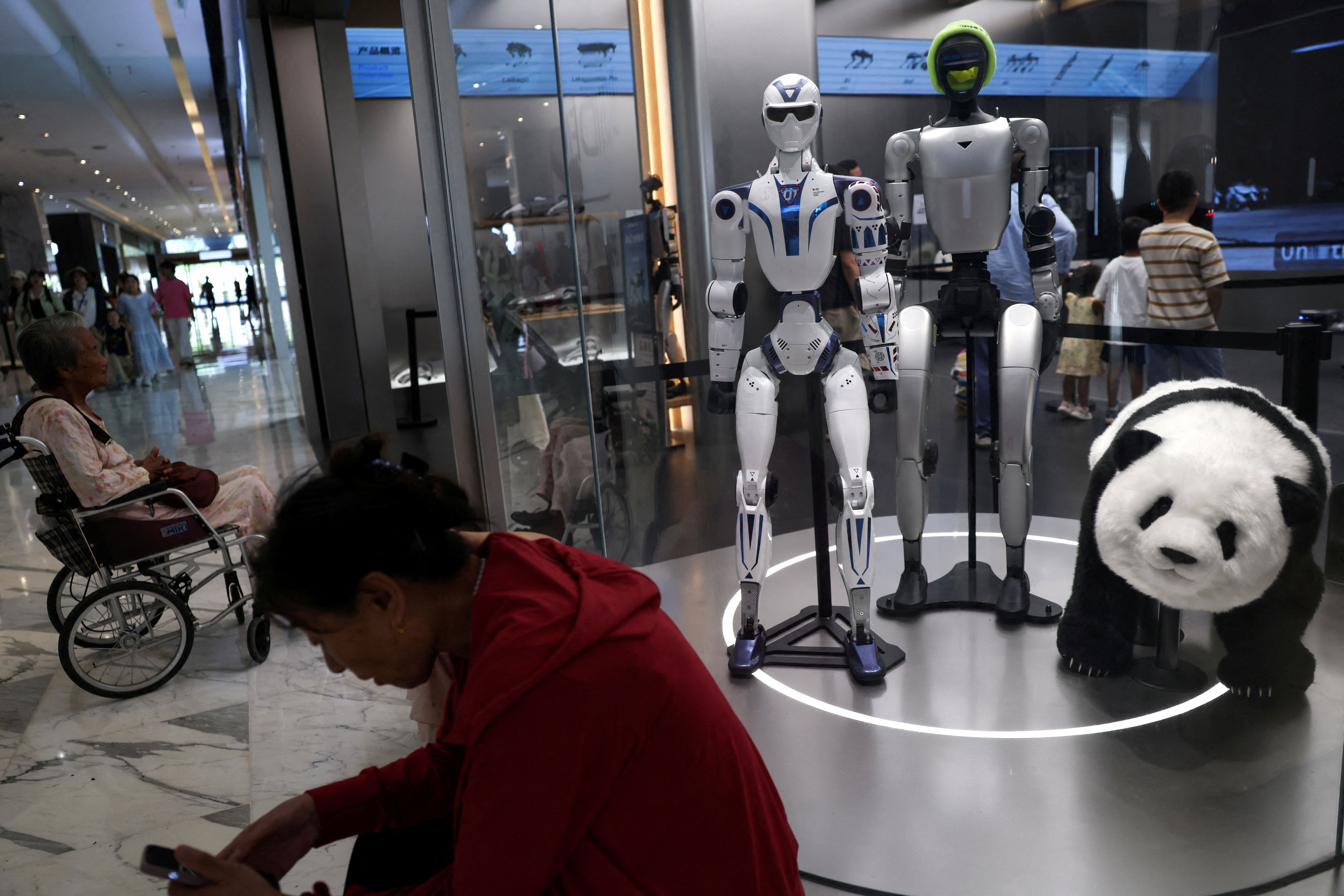 People rest near Unitree’s G1 and R1 humanoid robots on display at a Unitree store in Beijing, China 