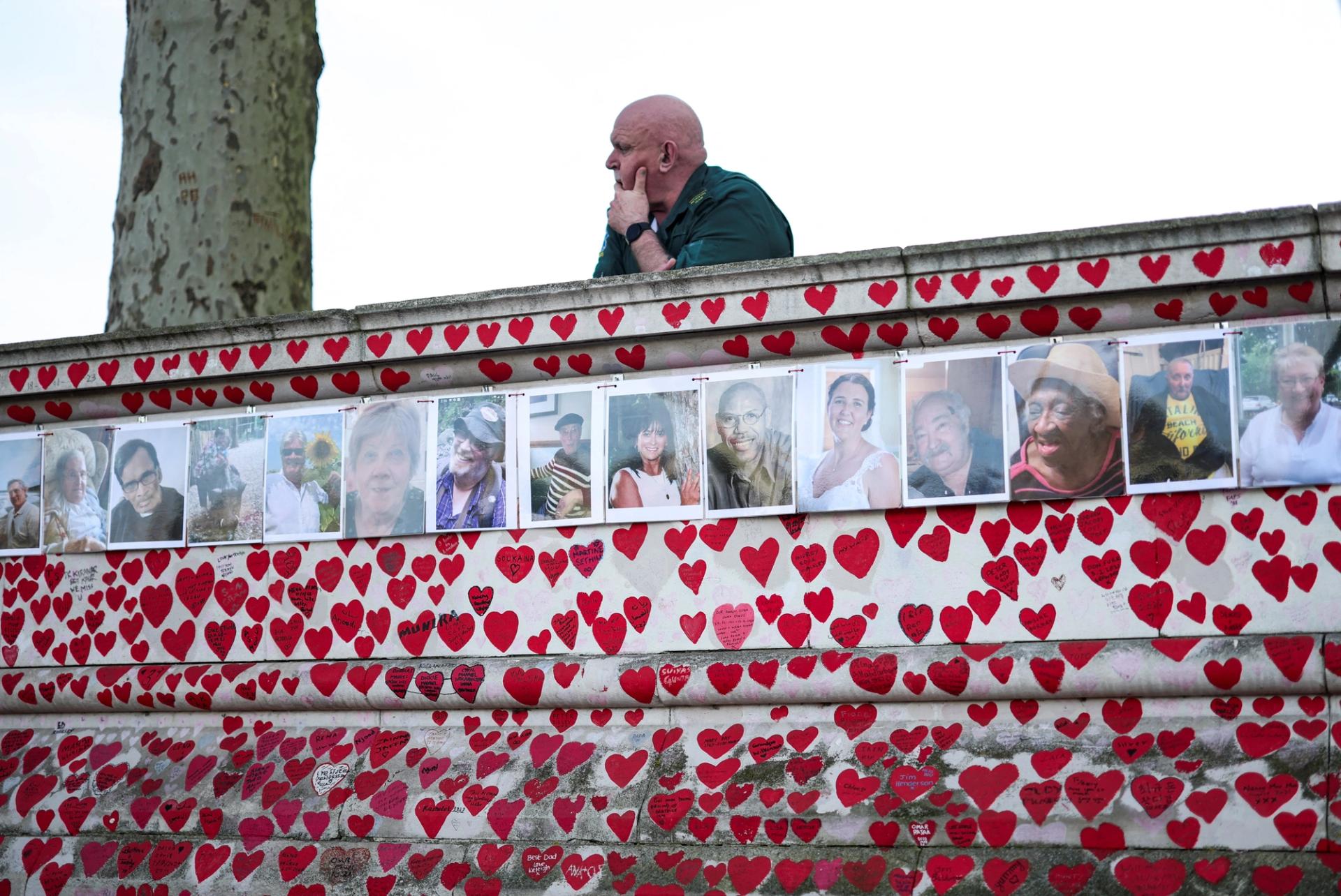 A man looks on near pictures of people who died because of COVID-19 in London.