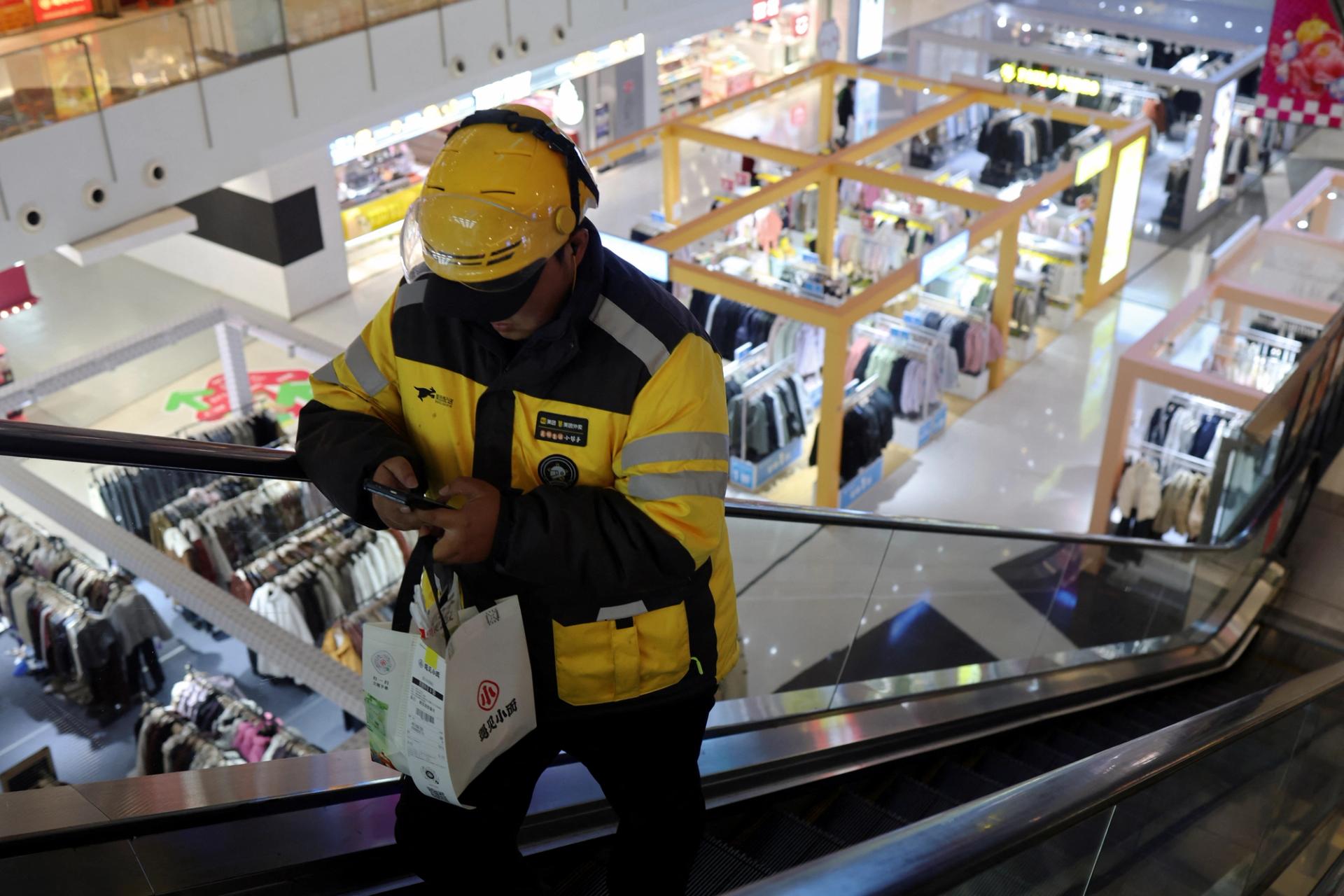 A Meituan delivery worker picks up a food order at a shopping mall in Beijing, China