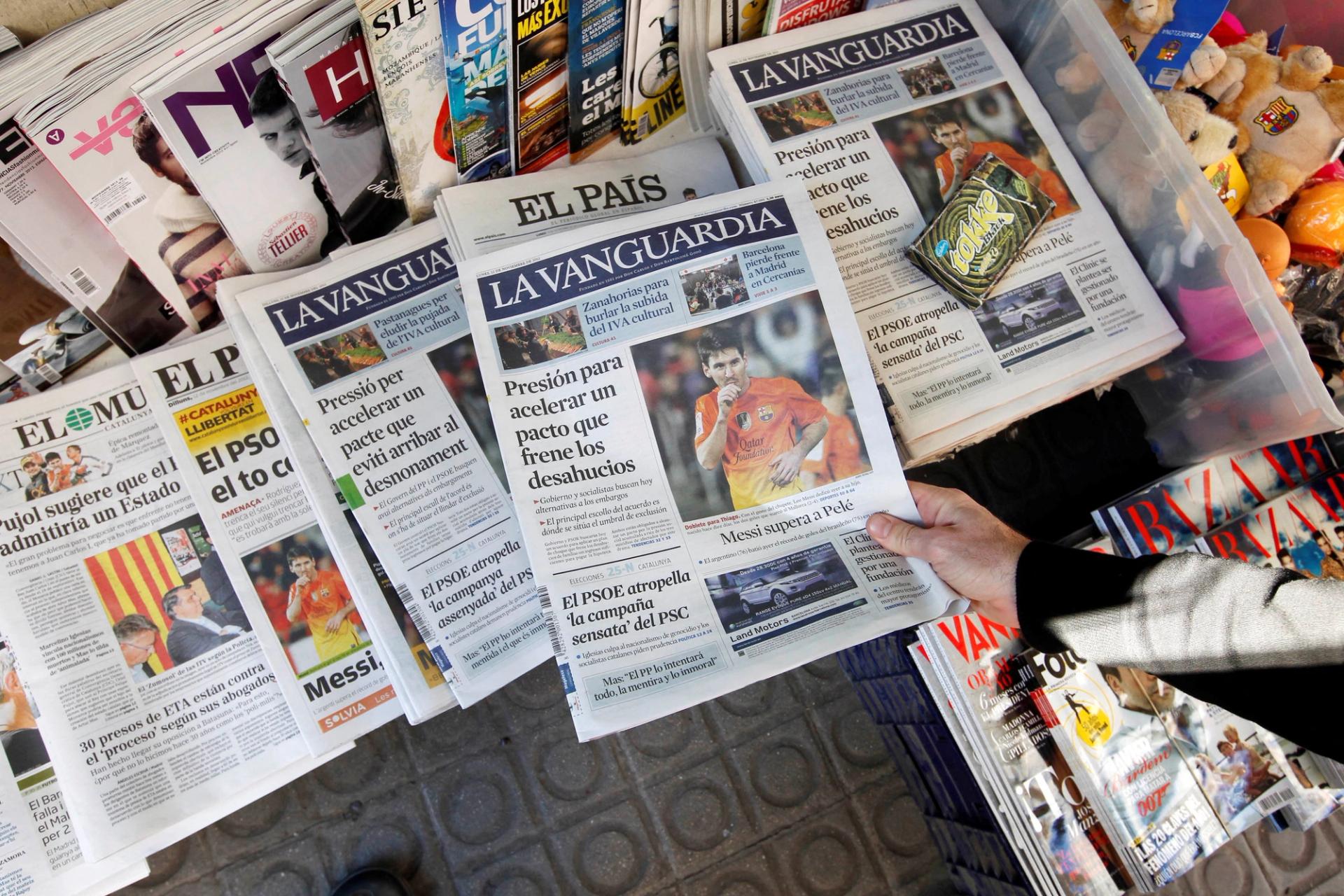 A person grabs a copy of the newspaper La Vanguardia written in Spanish placed next to a copy written in Catalan at Plaza de Catalunya in central Barcelona