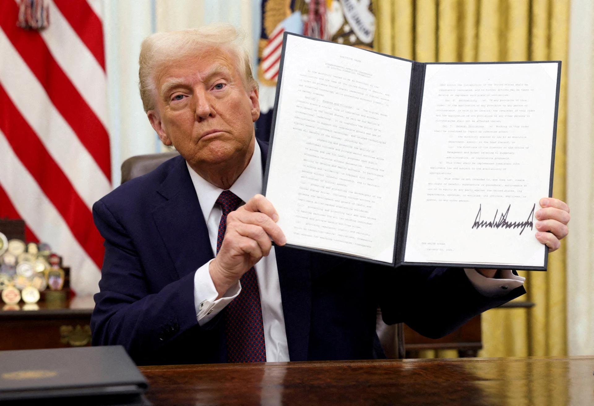 Donald Trump holds a signed executive order in the Oval Office. 