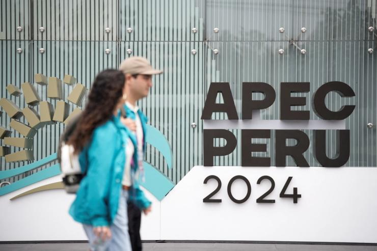 Two people walking in front of a building labelled APEC Peru 2024.