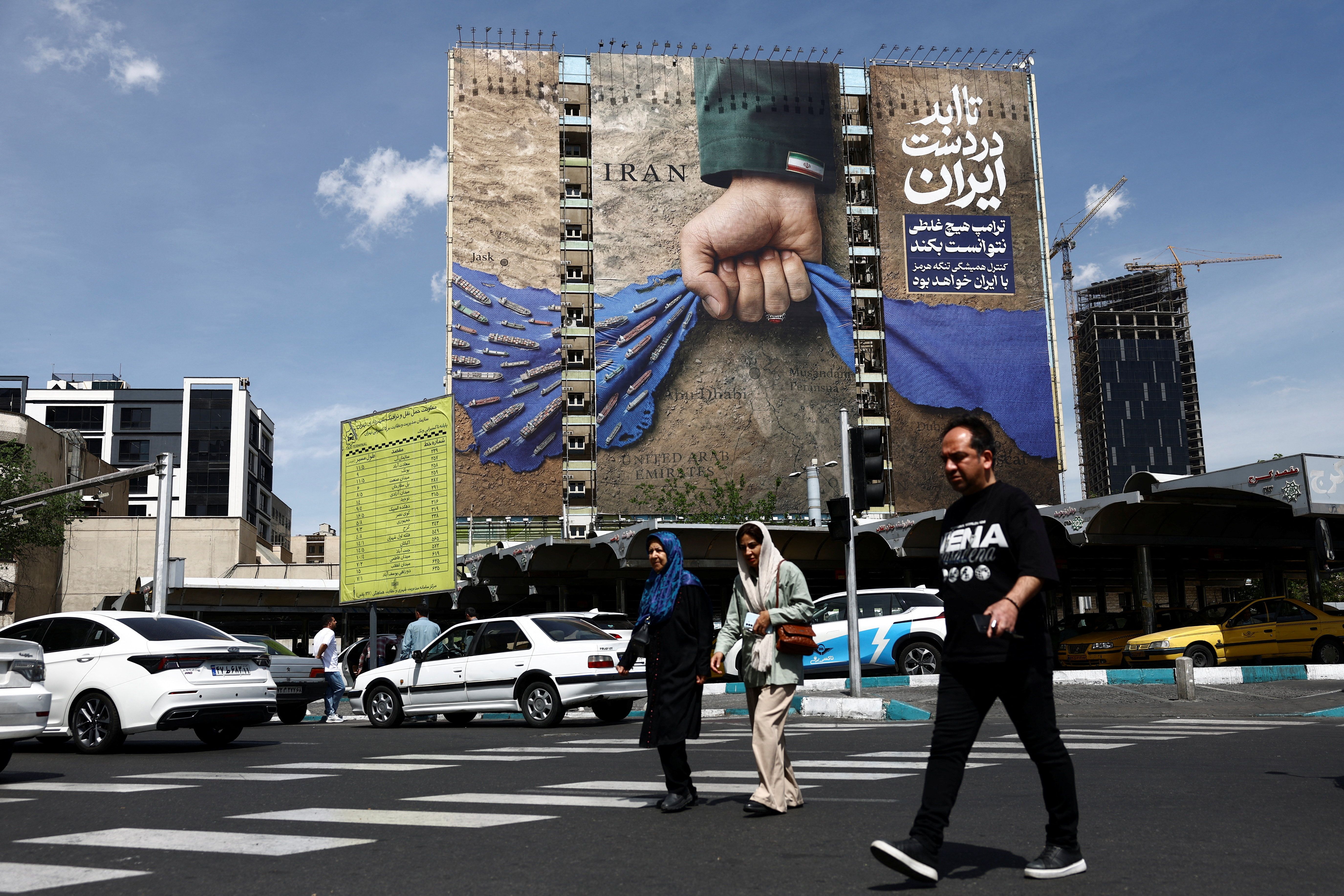 People walk past a billboard with a graphic design about the Strait of Hormuz on a building