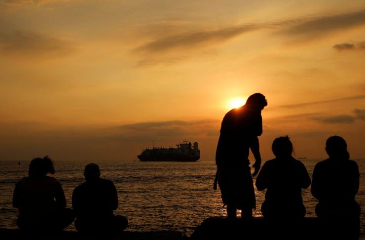 People sit near the BW Tatiana, a liquefied natural gas storage and regasification ship.