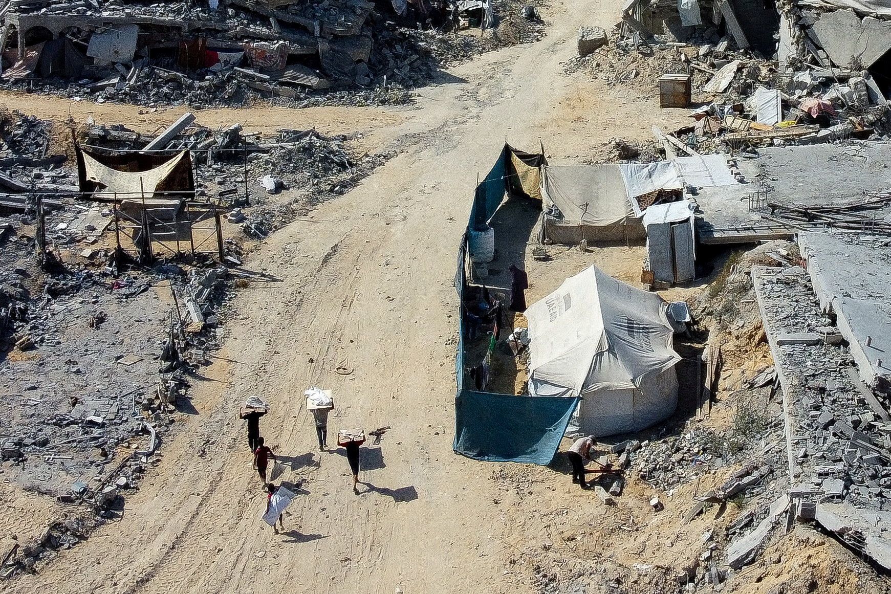Palestinians walk past a tent amid the rubble in a destroyed area, amid a ceasefire between Israel and Hamas in Gaza
