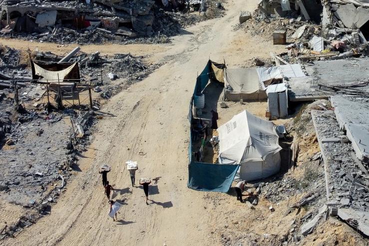 Palestinians walk past a tent amid the rubble in a destroyed area, amid a ceasefire between Israel and Hamas in Gaza