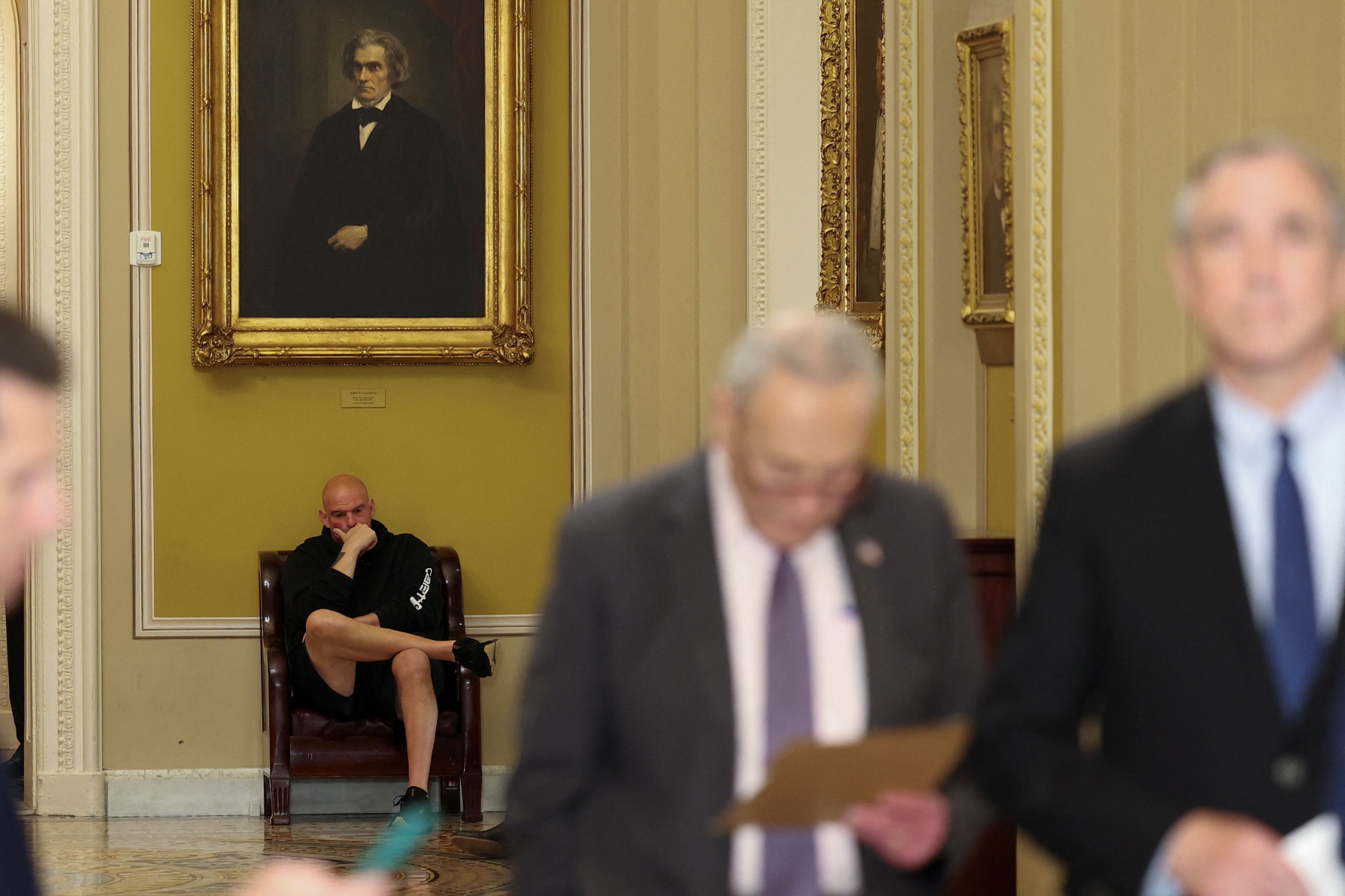 US Senator John Fetterman (D-PA) sits in the hallway behind Senate Minority Leader Chuck Schumer (D-NY) as he holds his weekly press conference following the Democratic caucus policy luncheon at Capitol in Washington, DC.