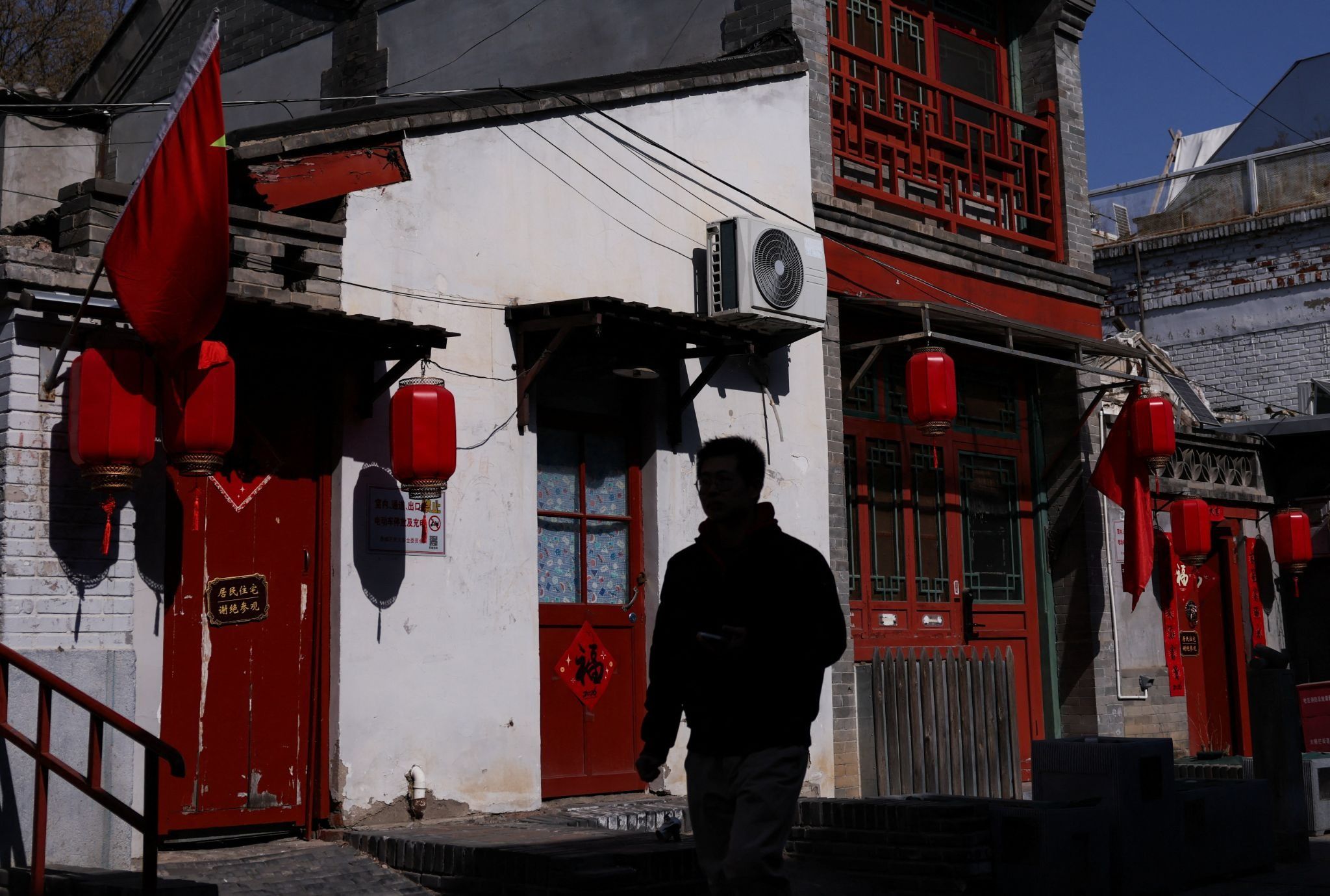 A person walks past a building with lanterns and Chinese flags.