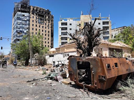 Sudan army members walk near a destroyed military vehicle and bombed buildings as some displaced residents return to the ravaged capital Khartoum in March 2025.