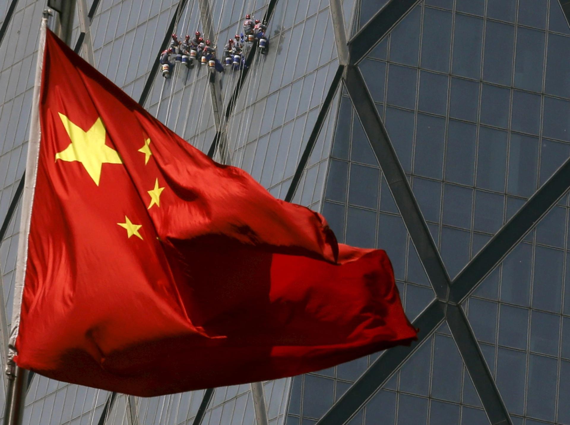 Workers cleaning the window of a tall building in a Beijing commercial district are seen behind China’s national flag.  