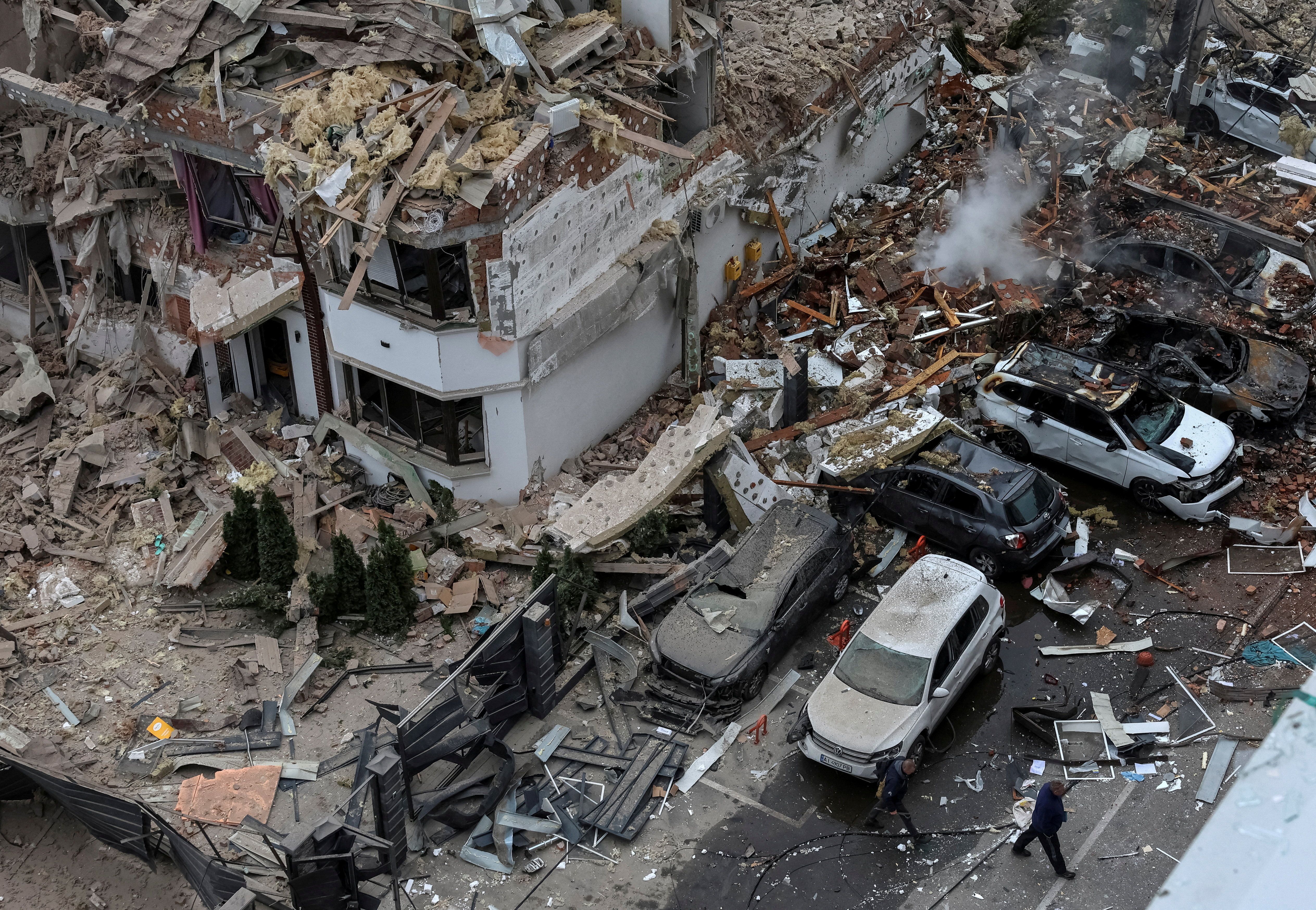People walk next to a damaged building and vehicles in a residential neighbourhood hit during a Russian drone and missile strike