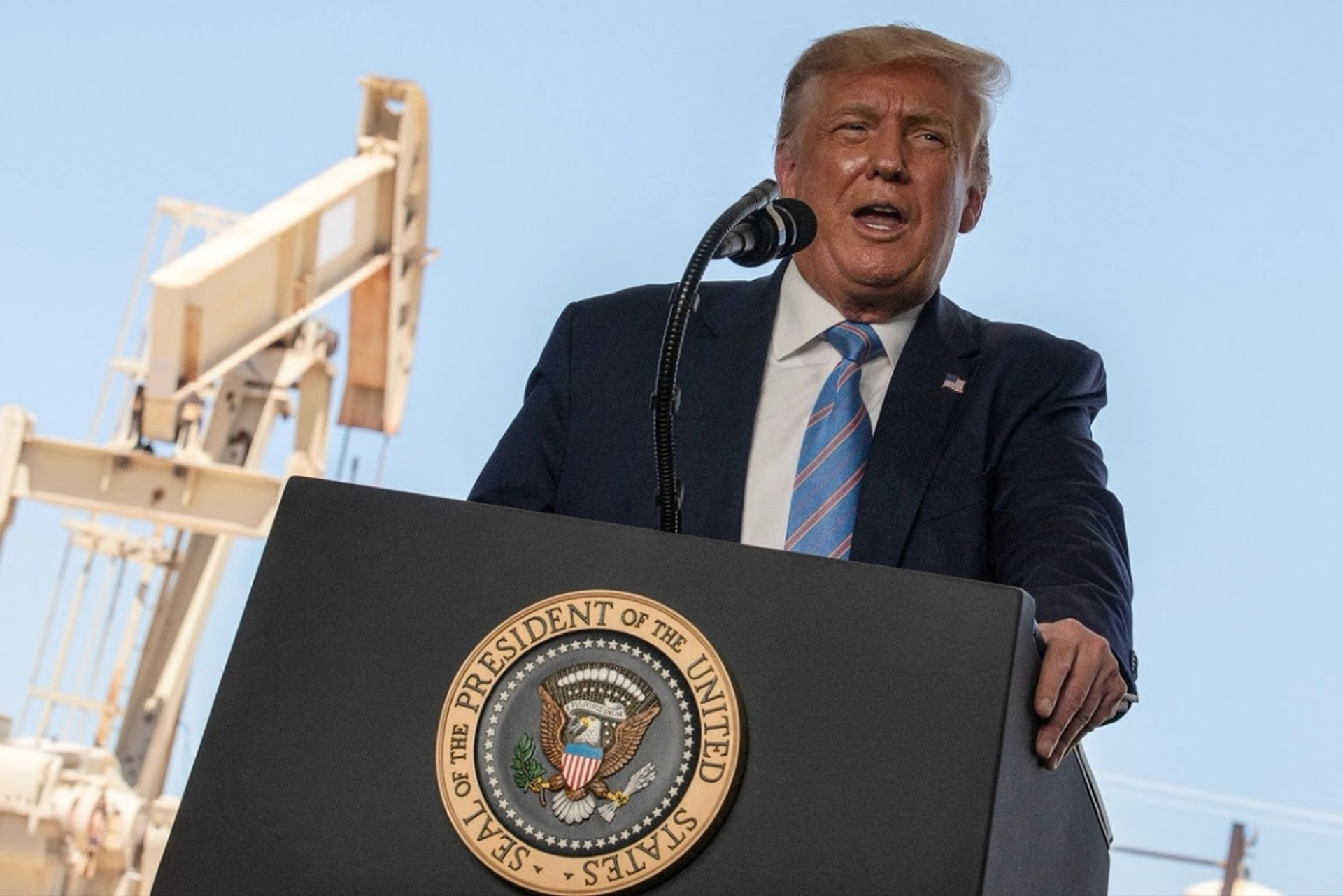 Donald Trump, wearing a dark suit and striped blue tie, gives a press conference