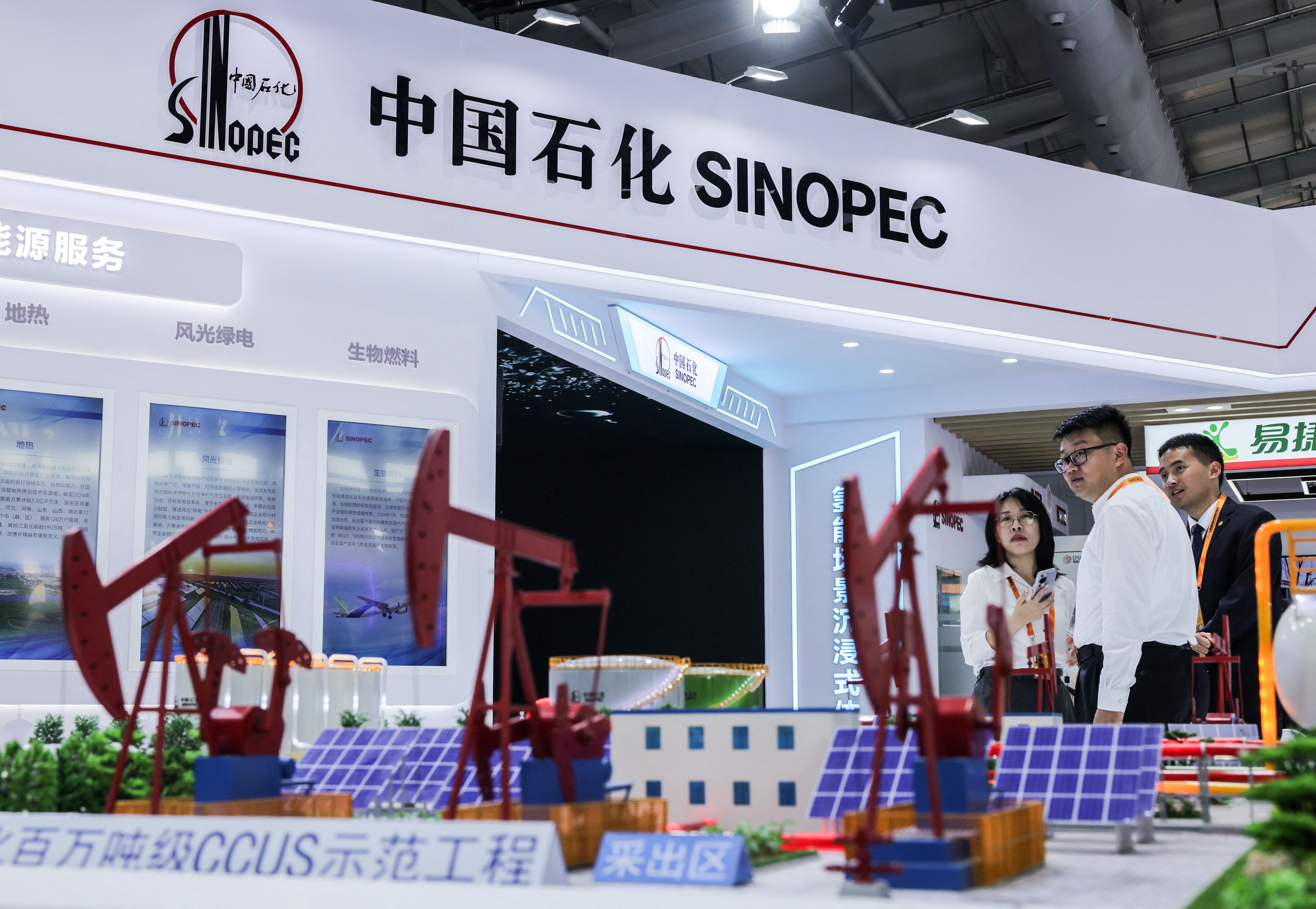 People look on with models of oil pump jacks seen in the foreground at China Petroleum & Chemical Corporation, or Sinopec, booth at China International Fair for Trade in Services (CIFTIS) in Beijing