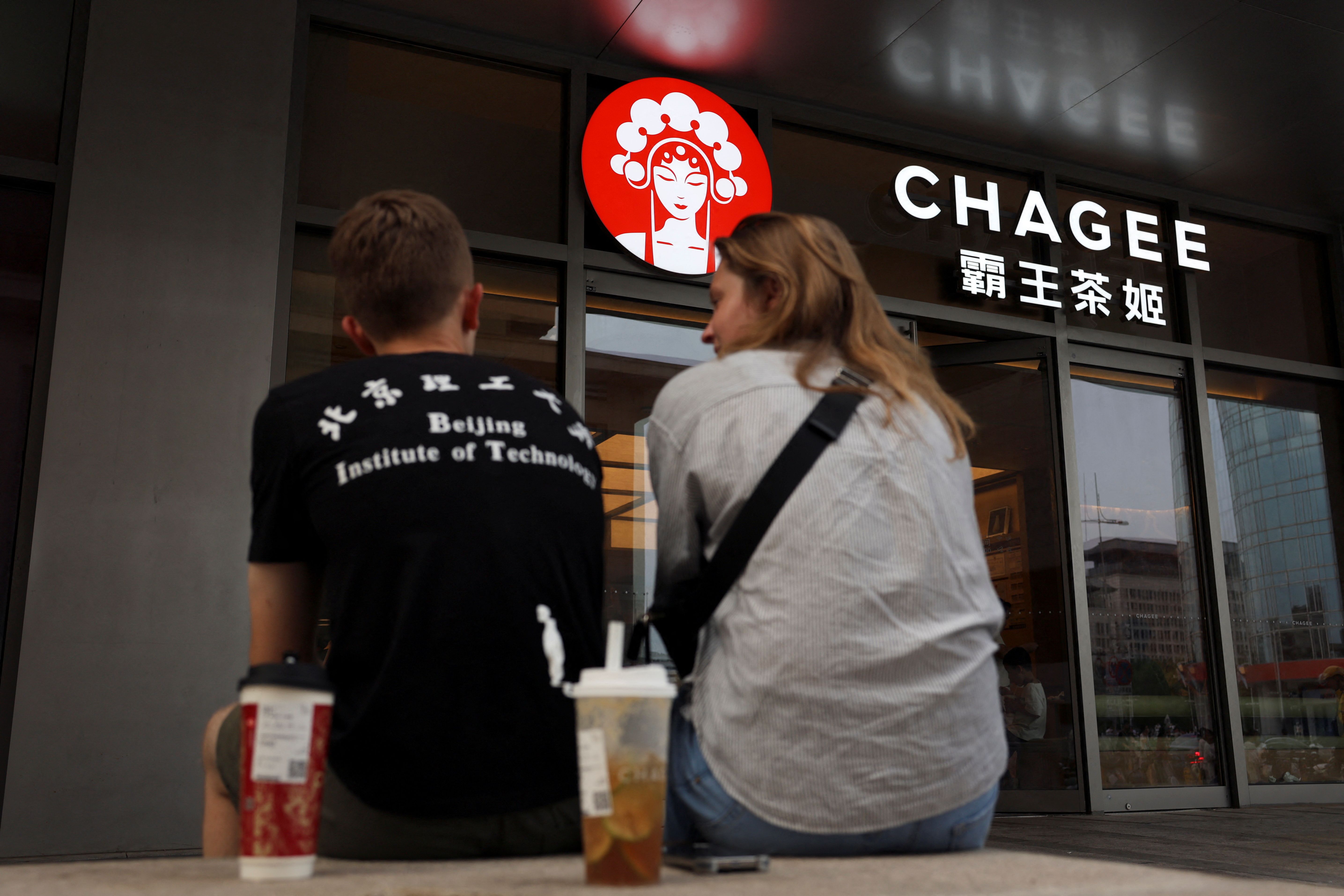 People sit outside a store of Chinese tea chain Chagee at a shopping mall in Beijing