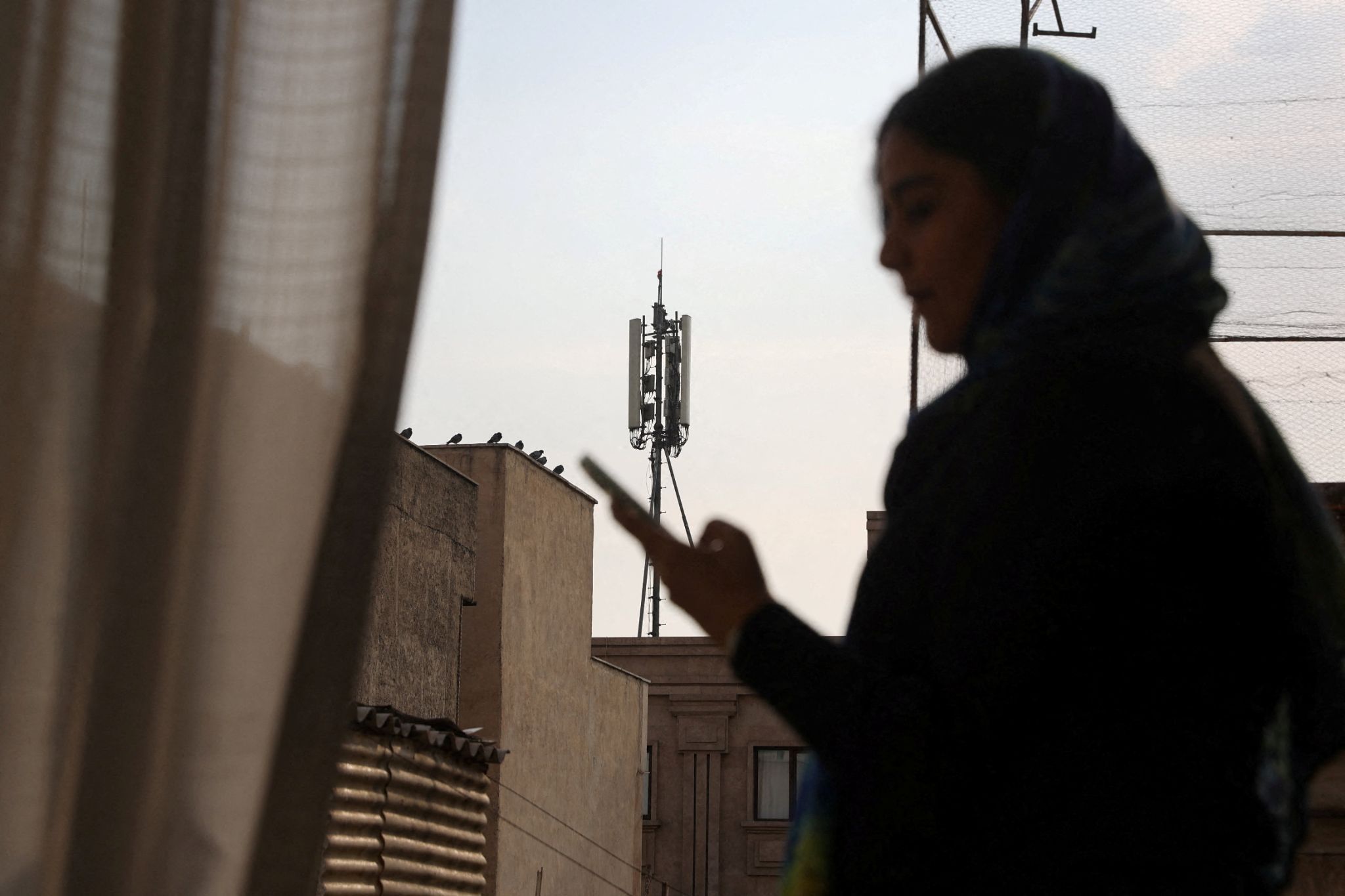An Iranian woman attempts to use a smartphone, a telephone tower in the background
