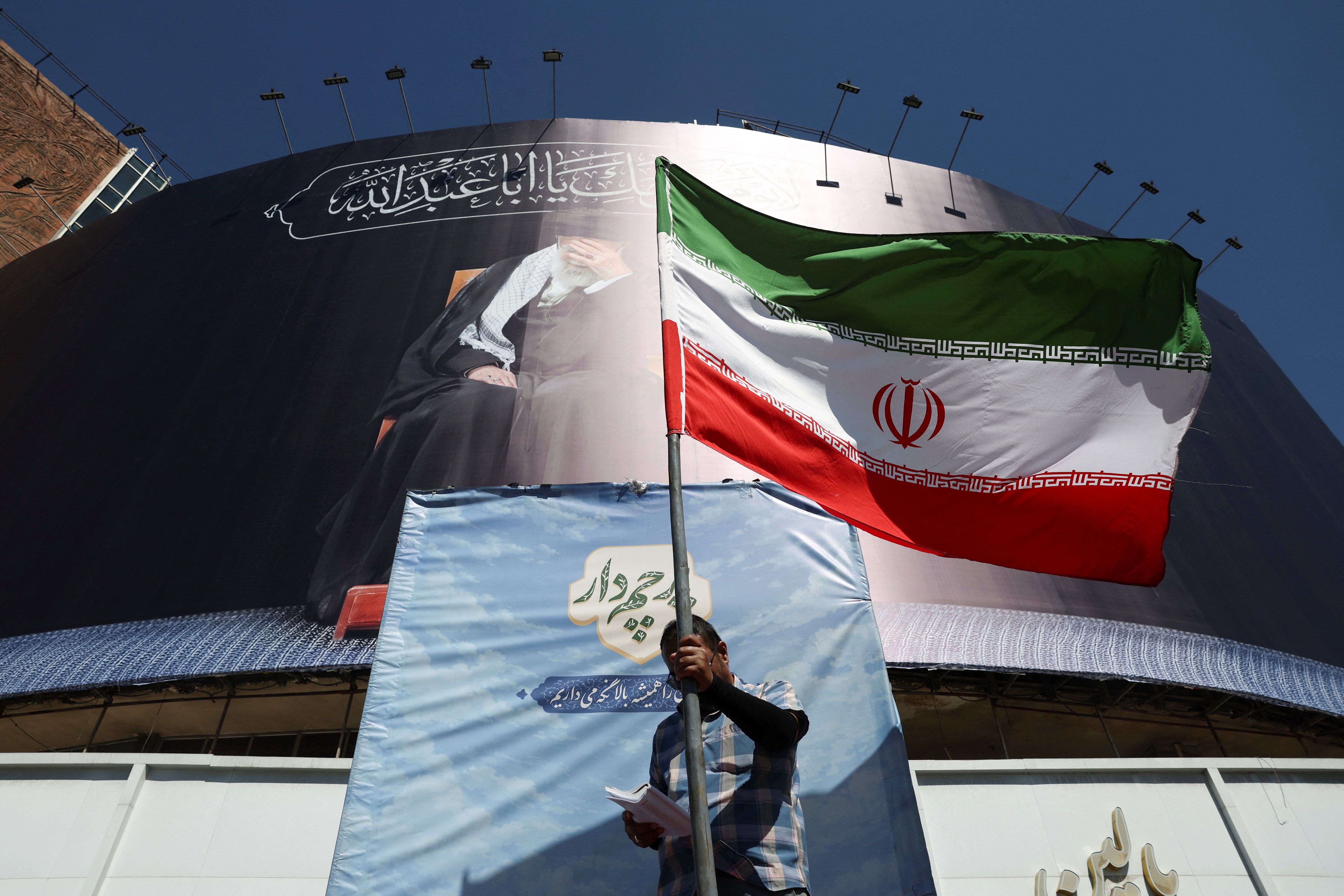 A man holds an Iranian flag on a street.