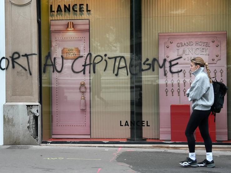 A woman walks past a Lancel store that was vandalised during clashes that erupted during a national day of demonstrations against the cost of living and rising fuel prices, in Lyon, France