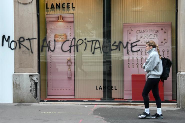 A woman walks past a Lancel store that was vandalised during clashes that erupted during a national day of demonstrations against the cost of living and rising fuel prices, in Lyon, France
