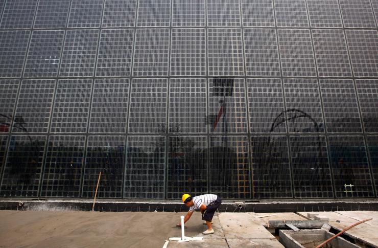 A worker smoothes out cement in front of a building covered in solar panels near the factory of Yingli Green Energy Holding Company, also known as Yingli Solar, in the city of Baoding.