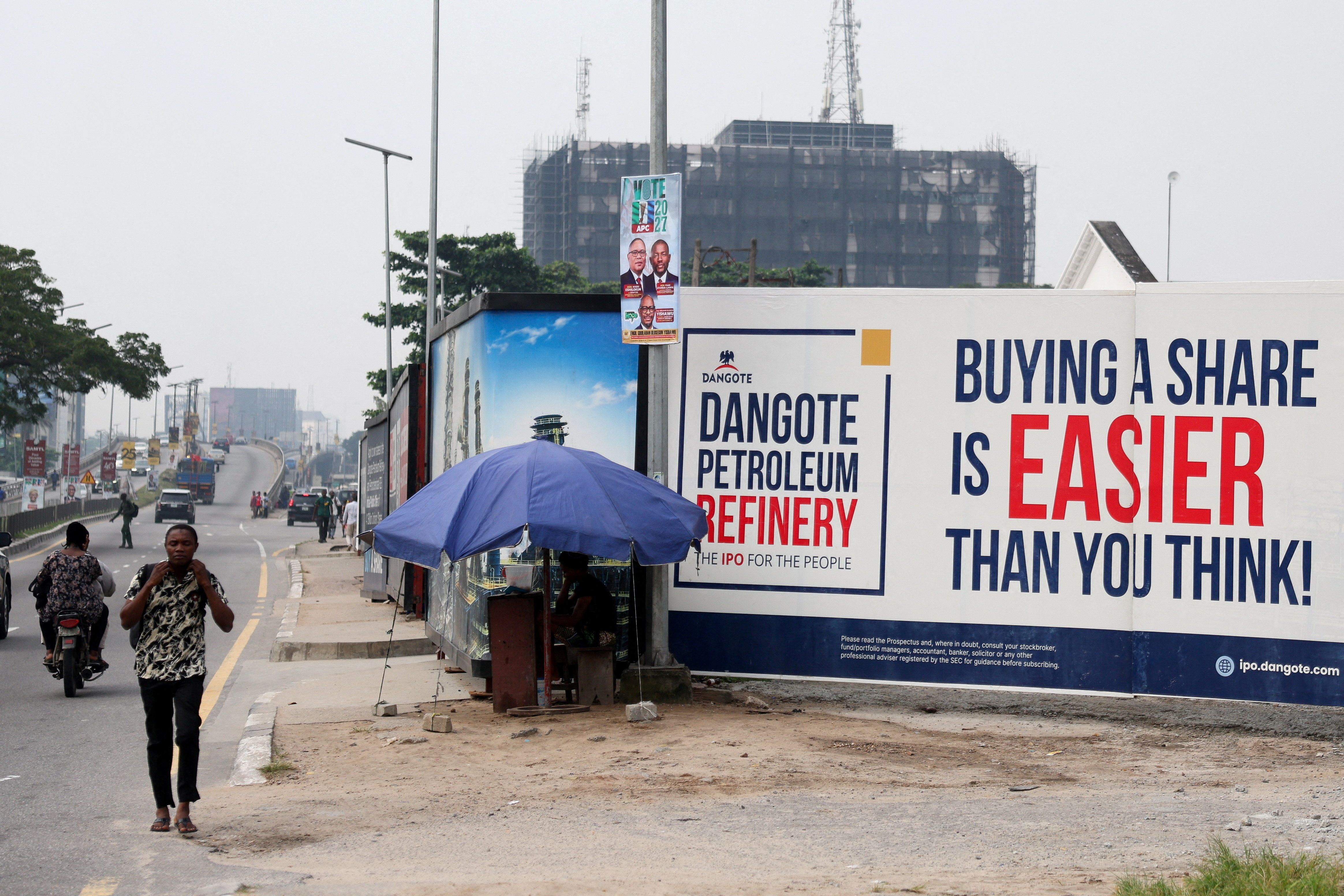 People walk near a billboard advertising Dangote Petroleum Refinery’s initial public offering.