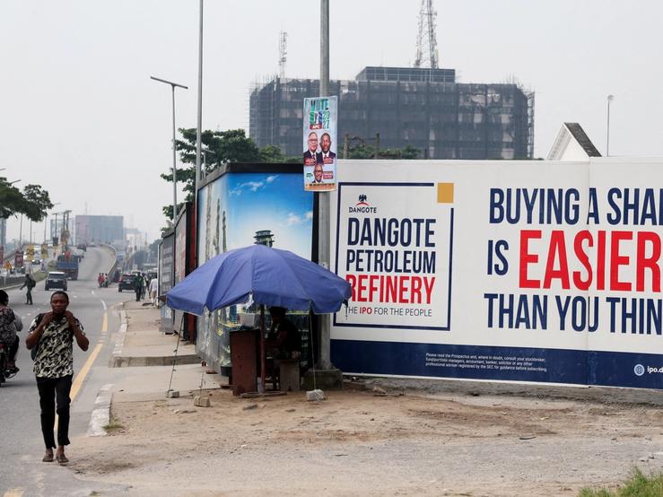 People walk near a billboard advertising Dangote Petroleum Refinery’s initial public offering.
