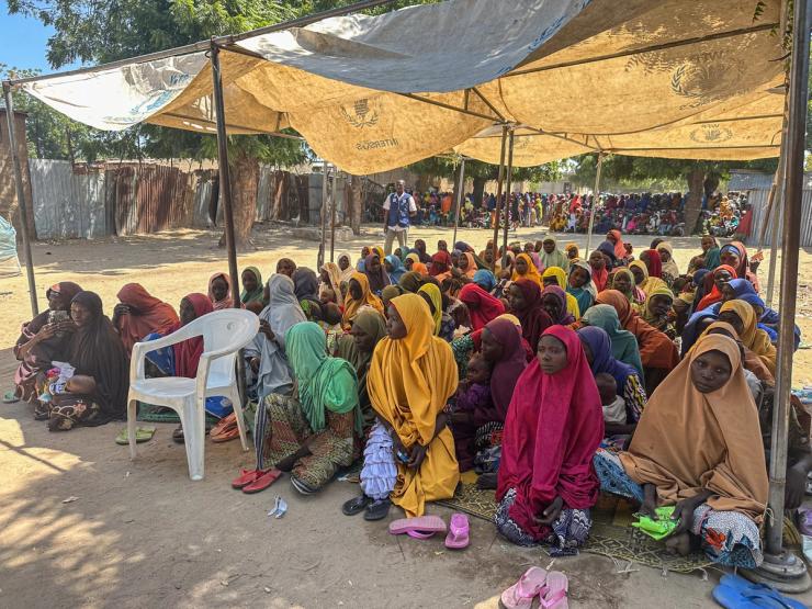 Dozens of women wait under a tarp to receive WFP food support in Maiduguri, Nigeria.