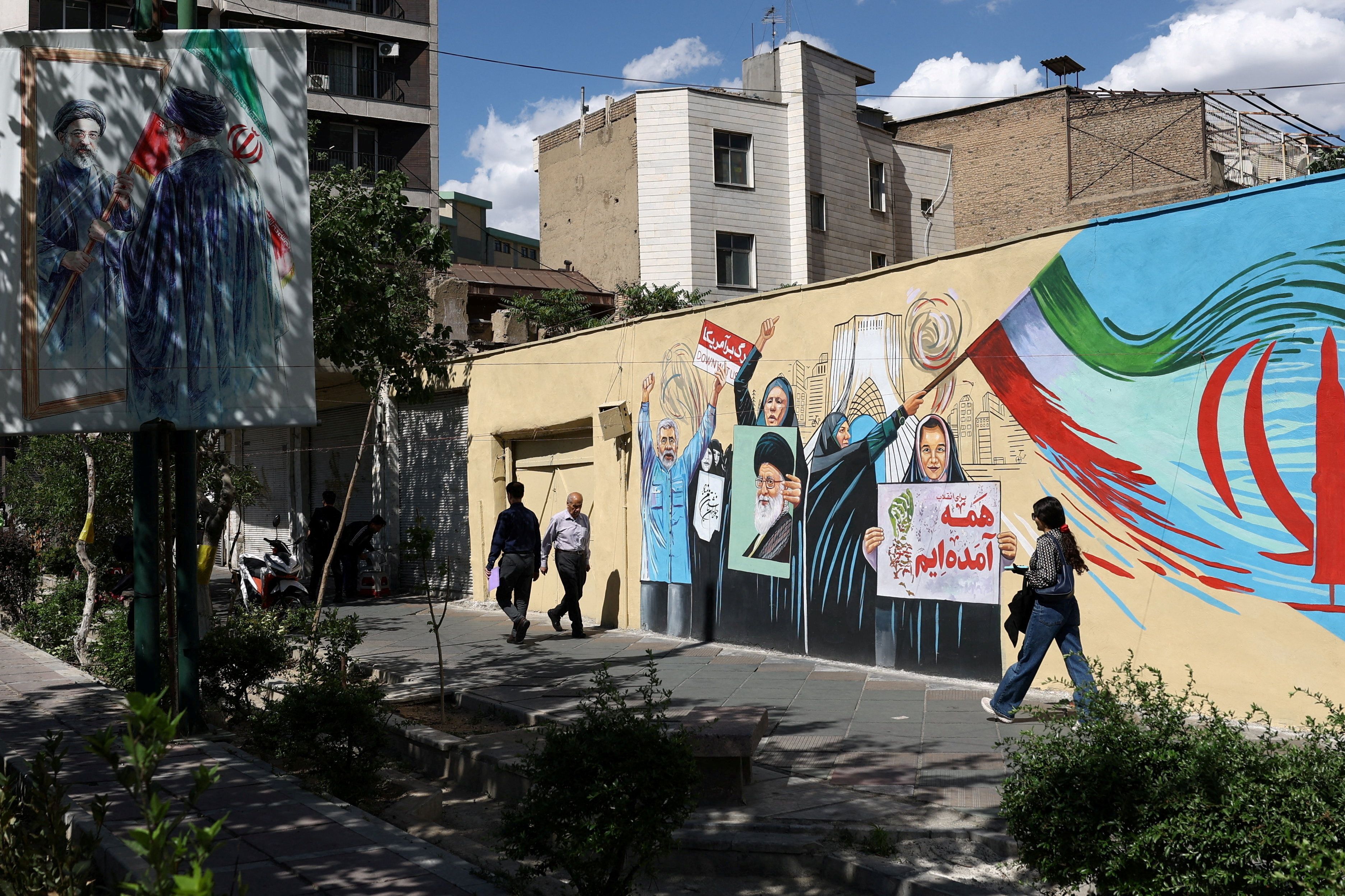People walk on a street near a mural featuring an image of the late Supreme Leader of Iran
