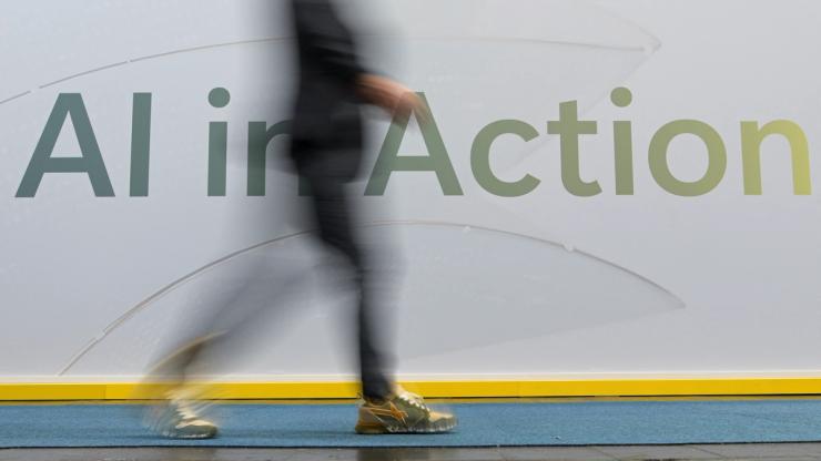 A person walks past a writing on the wall that reads “AI in Action” on the day of the Hannover Messe.